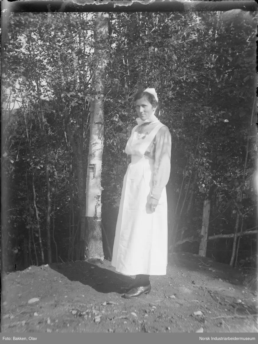 Kvinne i sykepleieruniform ved en bjørk.
