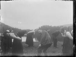 Mennesker i lek eller dans på gresslette ved Kyrkjetjønna.