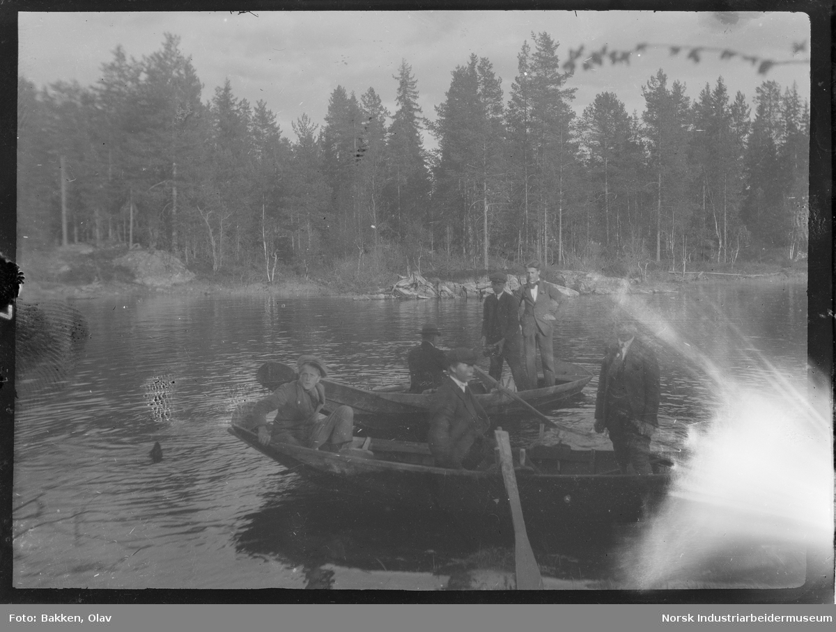 Gutter og menn stående og sittende i to robåter på vann.