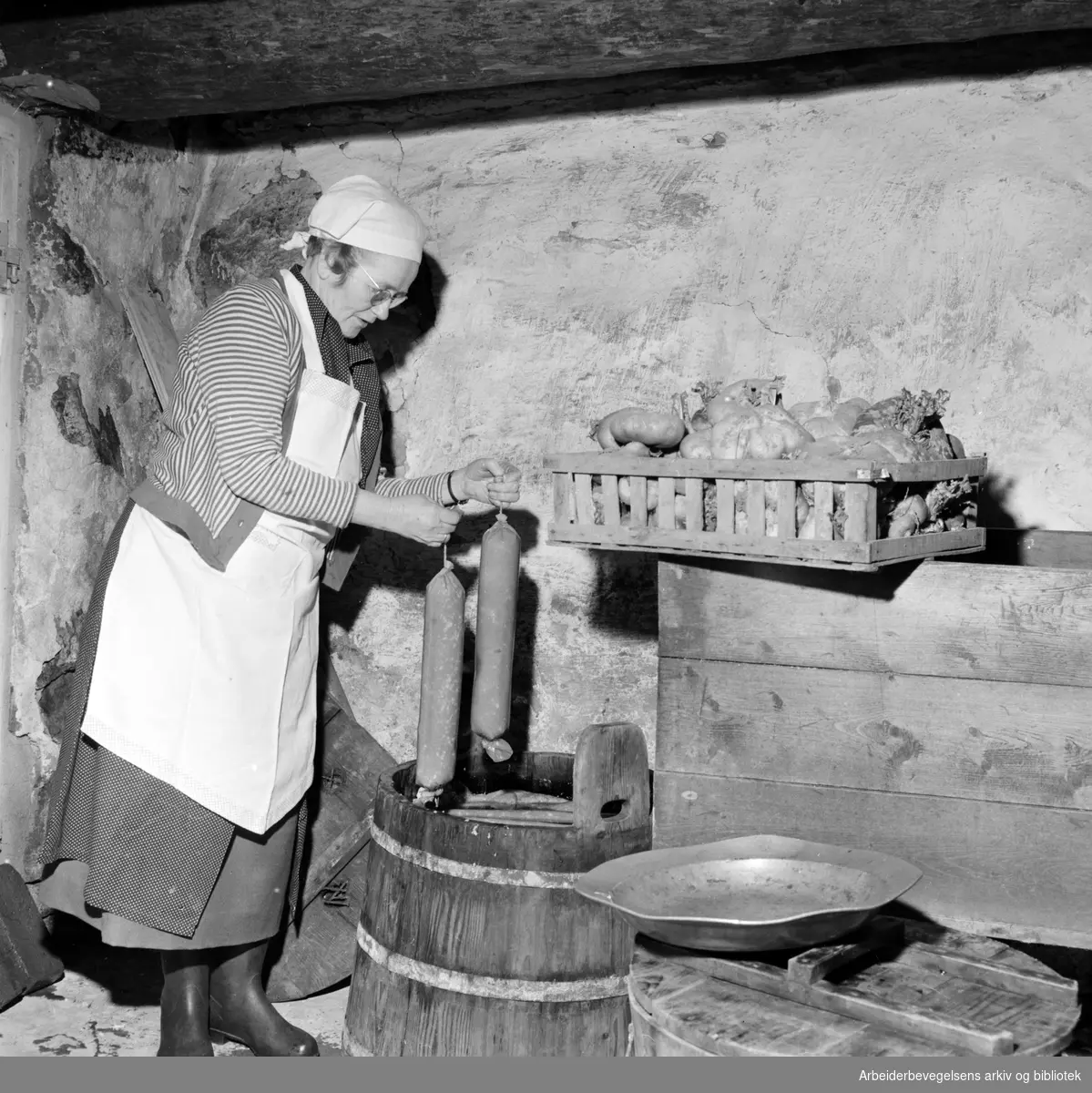 Juleforberedelser på Øvre Johnsrud gård i Lommedalen. Judith Johnsrud håndterer pølsene. Desember 1958.