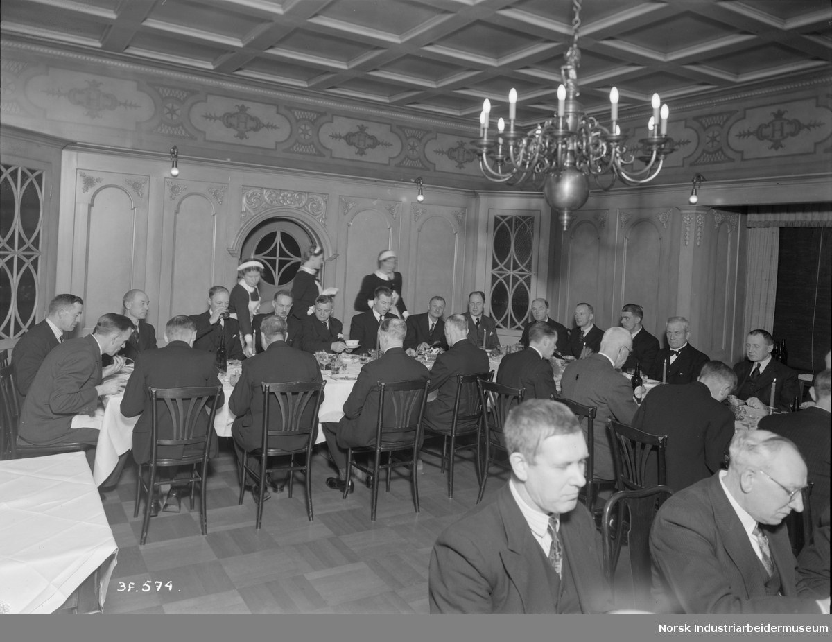 25. års jubilanter i Norsk Hydro 1939 og 1940. Middag på Administasjonsboligen. Serveringspersonale serverer mat ved bordene.