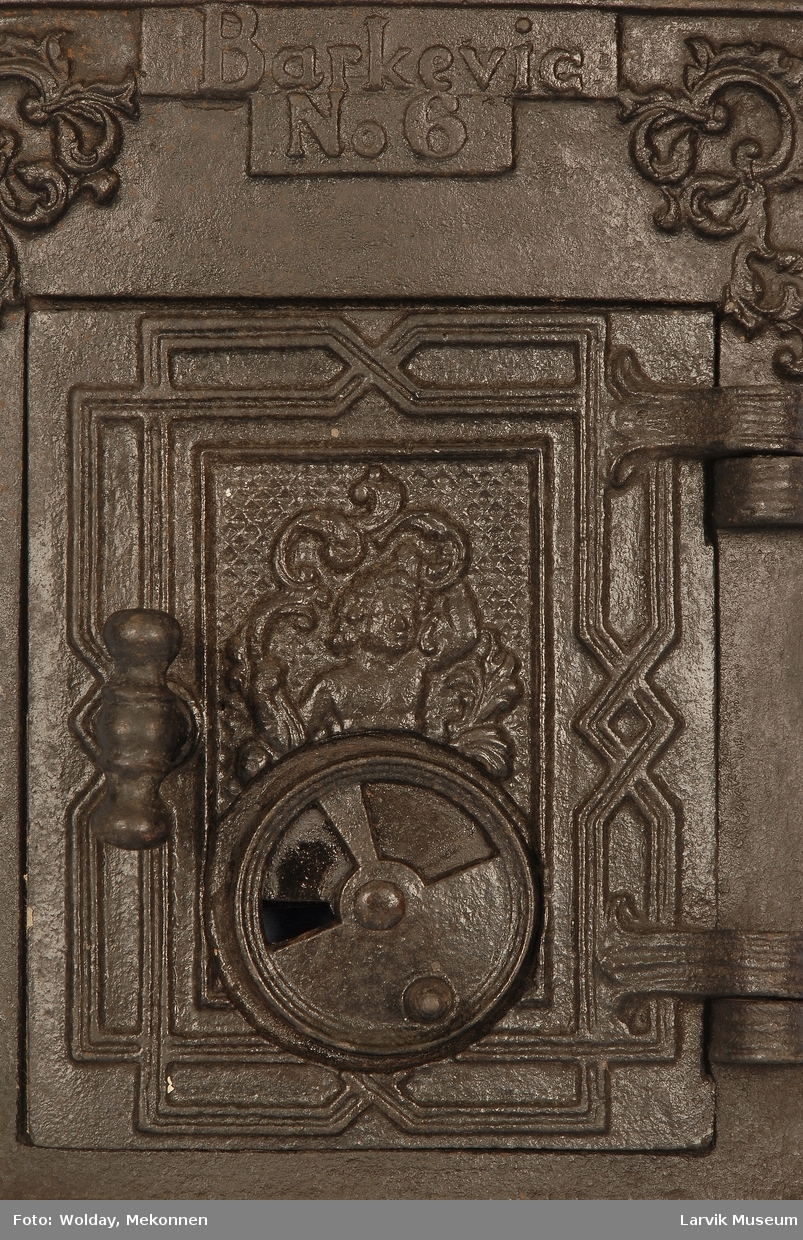 Midtstilt barnefigur omringet av acantus ornamentikk og todelt ramme på døren. Acantus ornamentikk i øverste hjørner