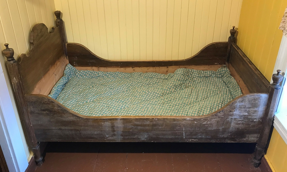 Brun seng  i tre med dekor på stolper og gavl.