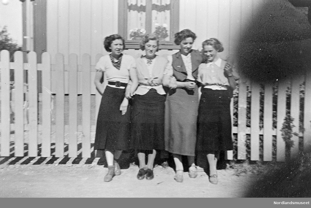 Anna Kristine Vatten, datter av Helga og Ole Vatten, sammen med 3 andre venninner. Hagegjerde og litt av bolighus i bakgrunnen. Gate i forgrunnen. Boligen med stående panel.
