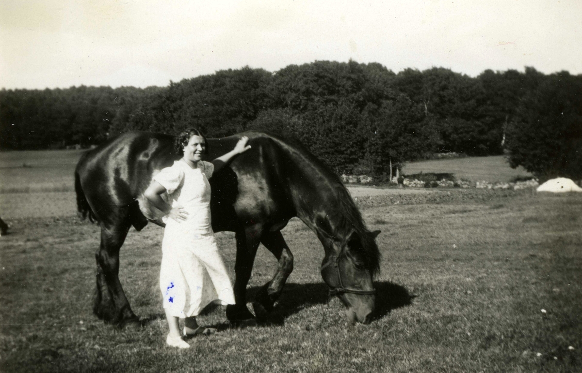 Linnea Dahlberg Fernlund (1910 - 1983) står vid hästen Bruno på en sommaräng cirka 1935. Sommargäst från Burås i Göteborg vid Tulebo Nordgård "Fredrikssons".