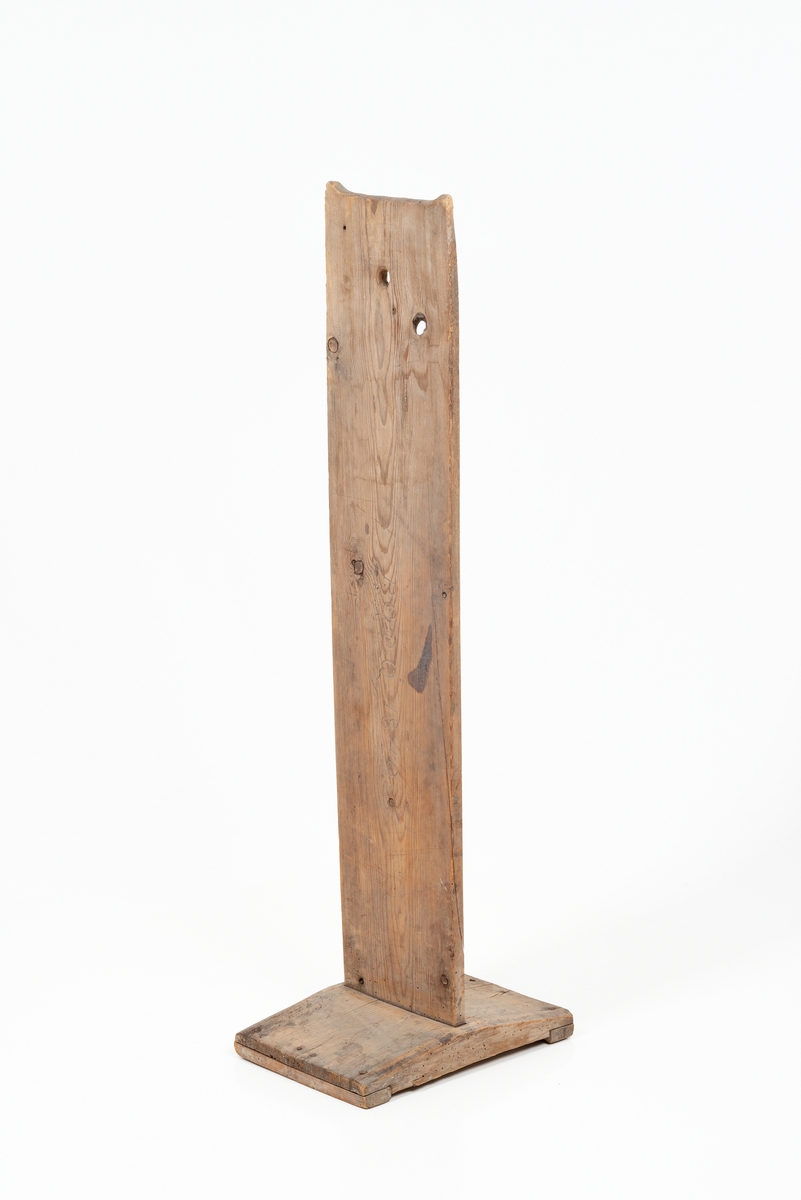Skakestol i tre. Rektangulær fotplate. Midt på fotplata er det festet et vertikalt trebord med innskrift. Trebordet har et kvisthull og et spikket hull.
