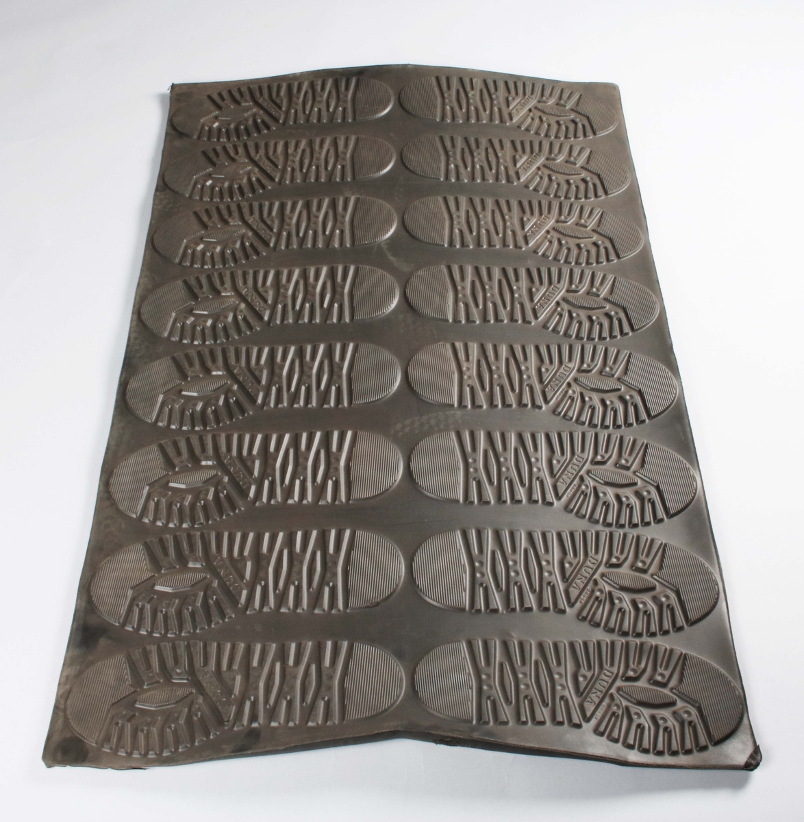 Rektangulär gummiplatta, med 16 gummisulor i relief, för tillverkning av skodon. 8 för höger fot och 8 för vänster fot. Färdiga för utstansning.
Sulorna märkta: DUNA Peuge