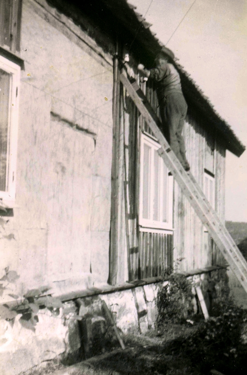 Erik Bengtsson (1899 - 1991) står på en stege vid renoveringen av bostadshuset Heljered Sörgård "Skräddarns" cirka 1950. Nya eternitplattor sattes upp och samtidigt byggdes en ny övervåning med en lägenhet till. Gården är riven och idag ligger Heljereds förskola på platsen.