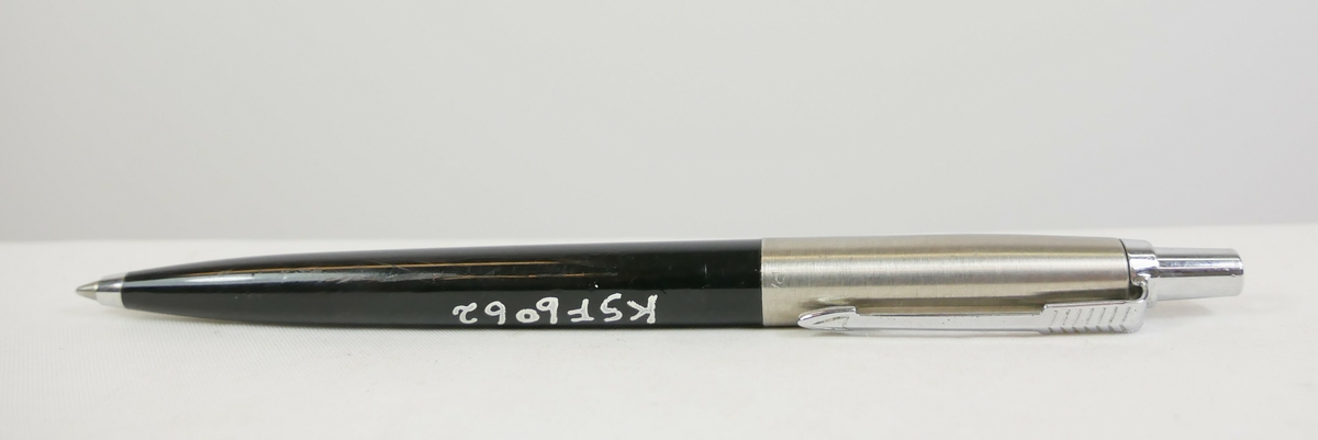 Fyllepenn med svart bunn og grå metall. På toppen er det en trykknapp og en metalldel til å feste med.