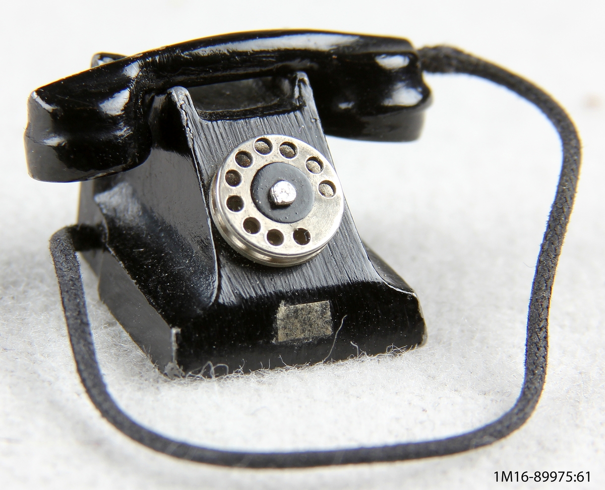 Telefon av metall, svartmålad, sifferskivan omålad. För dockskåp.