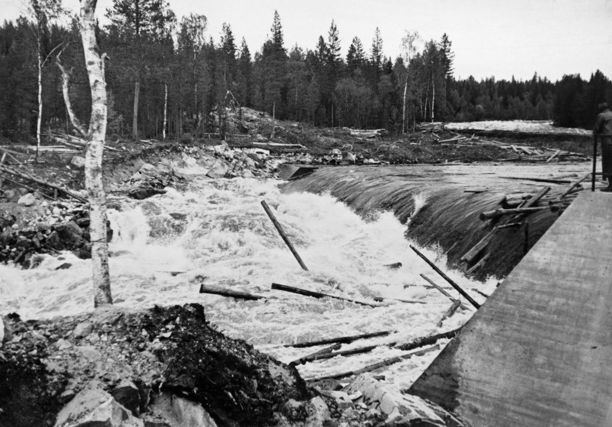 Kvernfallet i elva Søndre Osa i Åmot i Hedmark, fotografert i 1936. Bildet er tatt fra søndre elvebredd mot den da nybygdge terskeldammen, som skulle stuve opp vann til et nedenforliggende kraftverk. Bildet er tatt på et tidspunkt da det var betydelig vannføring i elvefaret. Bildet viser hvordan fløtingstømmeret fløt over damkrona og falt ned i det kvitskummende strømkavet under dammen, før det fløt videre med elvestrømmen.