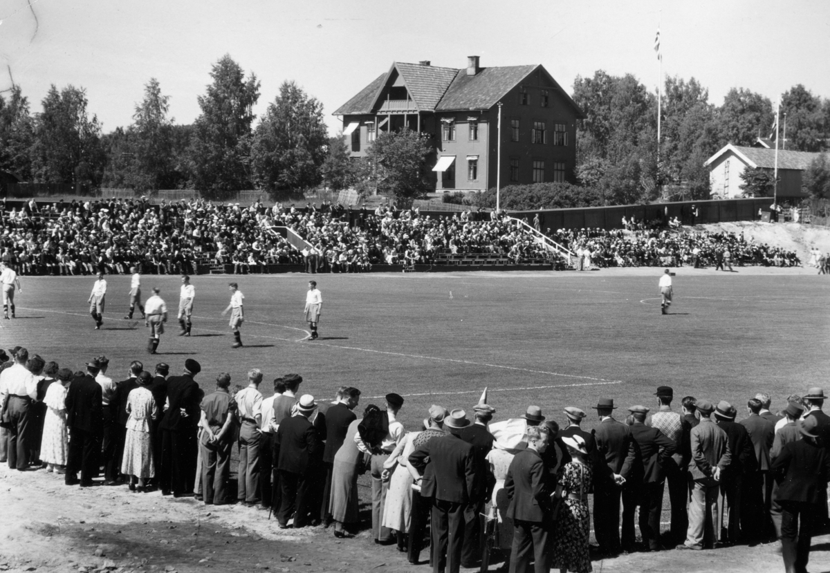 Briskeby Gressbane, Hamar. Åpningskamp 28.06.1936. Briskebyen fotballag spilte mot Lyn, Oslo og det var 2500 tilskuere. Fredvang skole. i bakgrunnen.