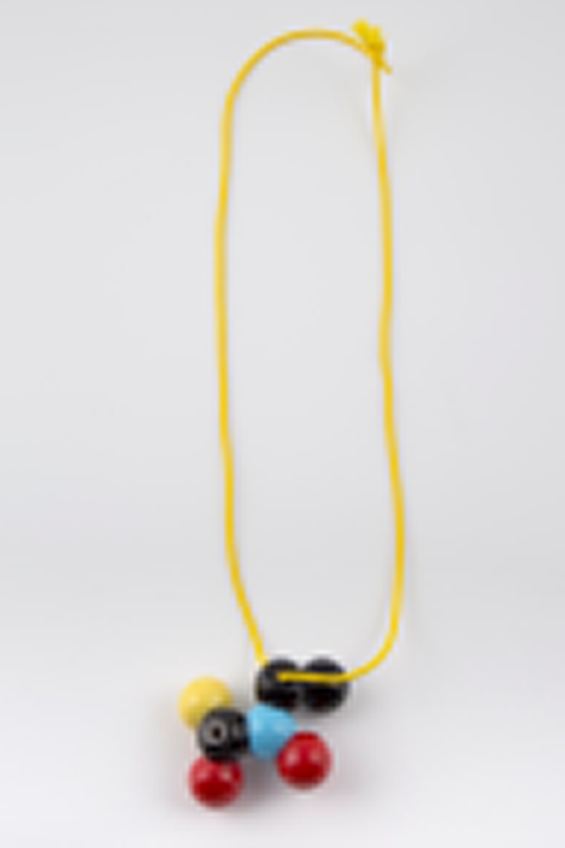 Halssmykke med gult kjede av gummitråd og et anheng i emaljert kobber. Anhenget består av en klynge kuler i primærfargene rødt, blått og gult samt svart.