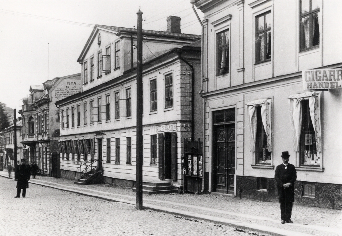 Kungsgatan, Växjö, med kvarteret Unaman, 1910.  I mitten av bilden den s.k. Schanderska fastigheten (kv. Unaman nr 3), hitom den hörnhuset (den s.k. P.N. Perssons hörna) mot Storgatan. I bakgrunden syns järnhandlare Sven Johan Johanssons fastighet med Nya Järnboden.
