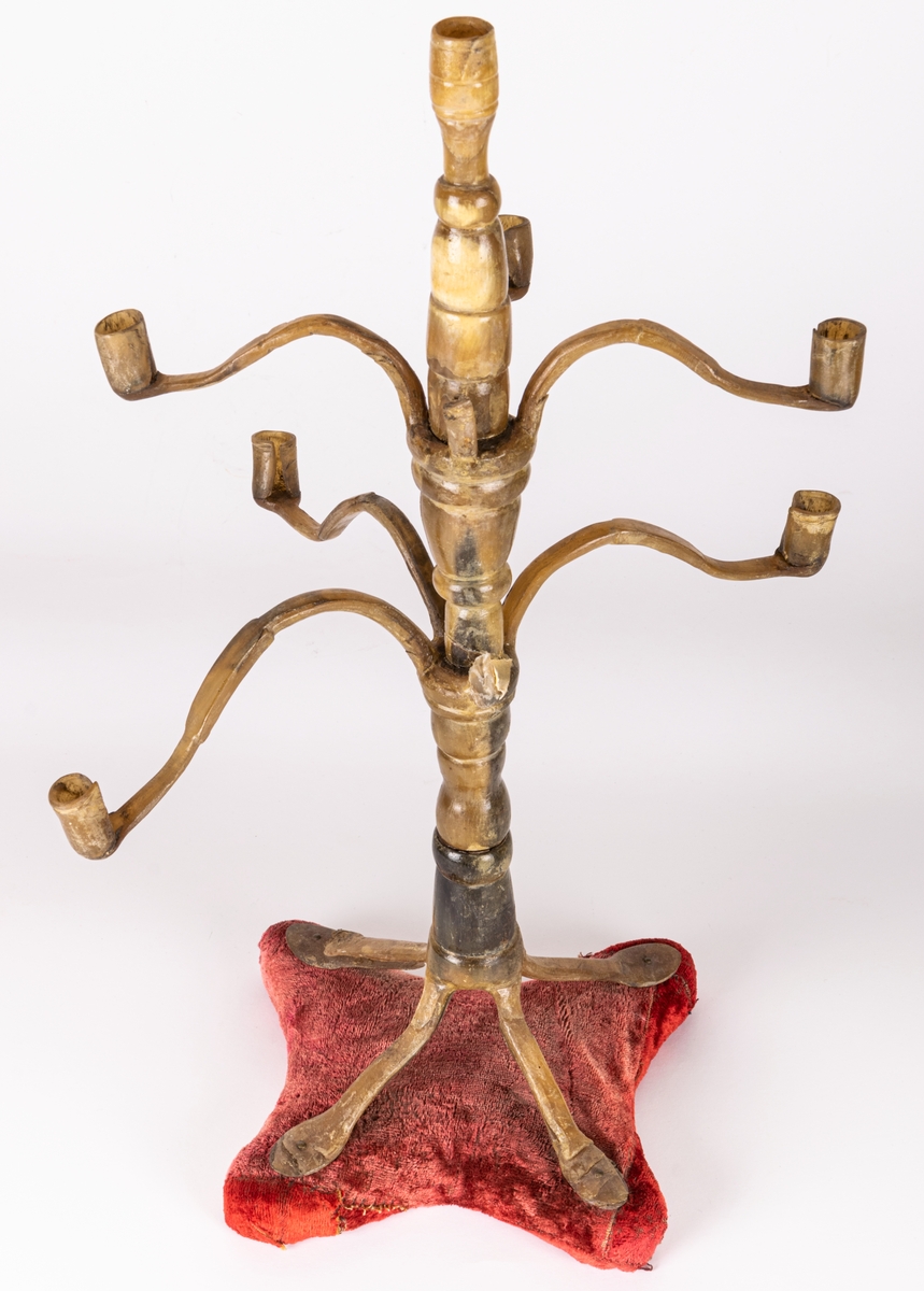 Ljusstake av horn, 9-armad (en arm borta), står på röd sammetsplatta.