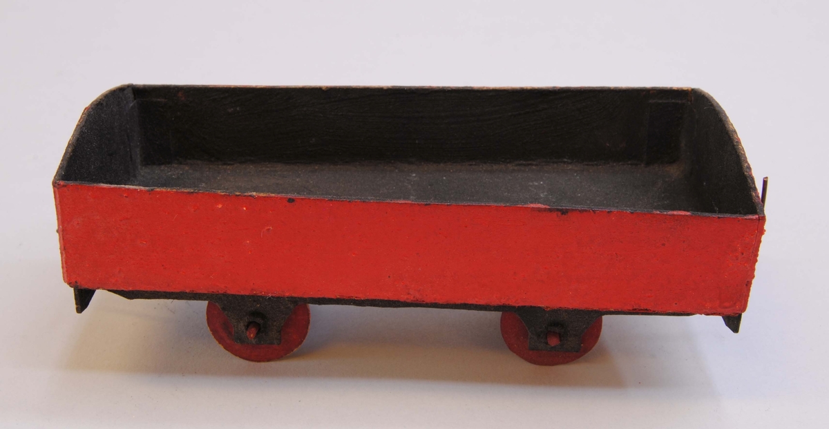 Öppen godsvagn av papp. Delarna är limmade eller sammanfogade med rött lack.
Hjulen är gjorda av papp och hjulaxlarna av fyrkantiga träpinnar, troligtvis tändstickor. Vagnen är målad röd på utsidan med svart insida, svart underrede och röda hjul.
Under vagnen är datumet "22/3 1920" handskrivet. På ena kortsidan av vagnen finns en ögla och på andra sidan en hake av ståltråd för att koppla samman vagnen med andra vagnar eller lok.