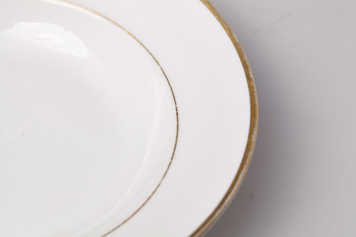 Suppetallerken i hvit porselen. Dekorert med gullkant og gullstripe i overgangen til mansjetten. Produsert av Porsgrund Porselen i 1958. 