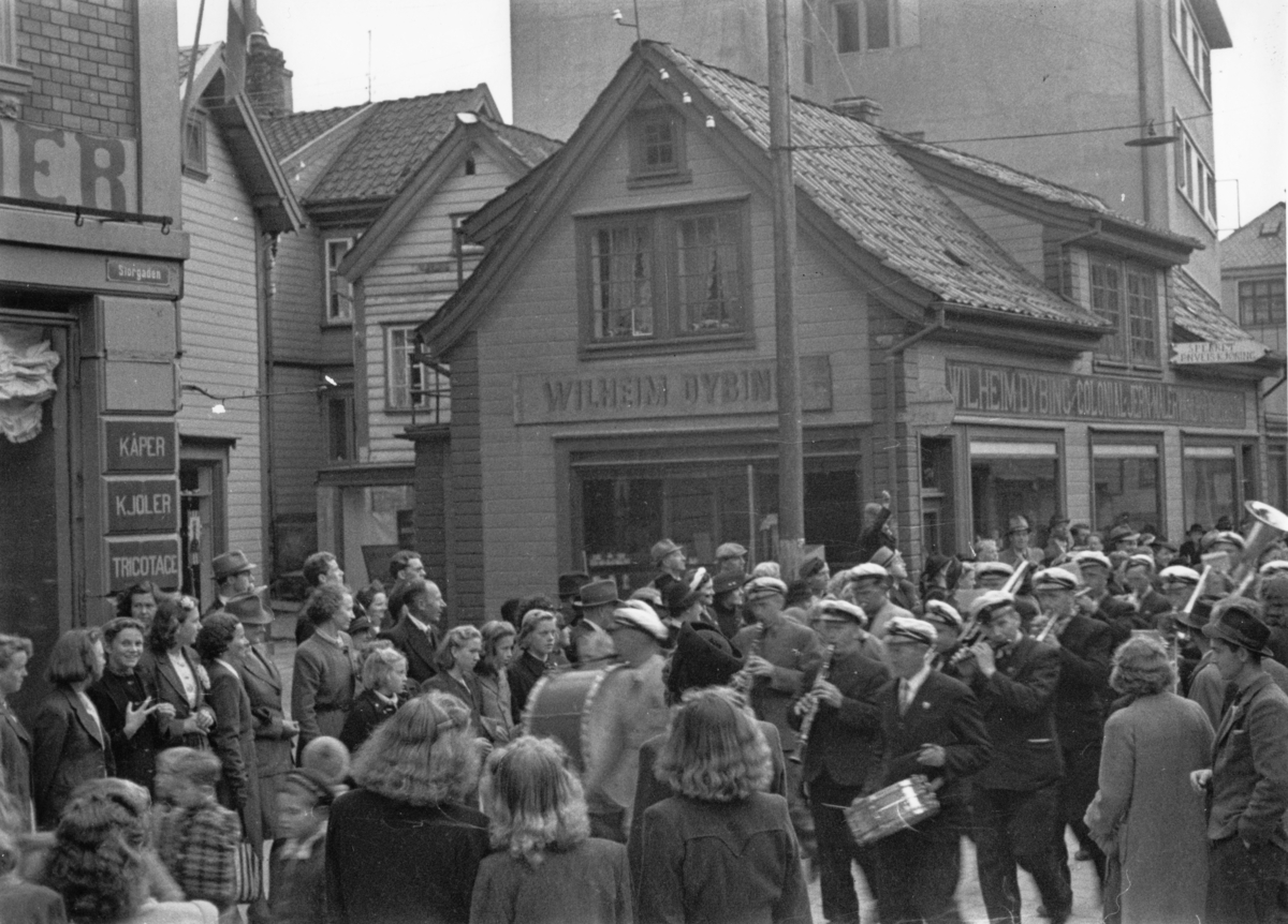 Storgaten, 30. mai 1945. Med musikk i spissen føres Arne Friestad fra torget og hjem. Her passerer de Dybings forretning i Storgaten 16.