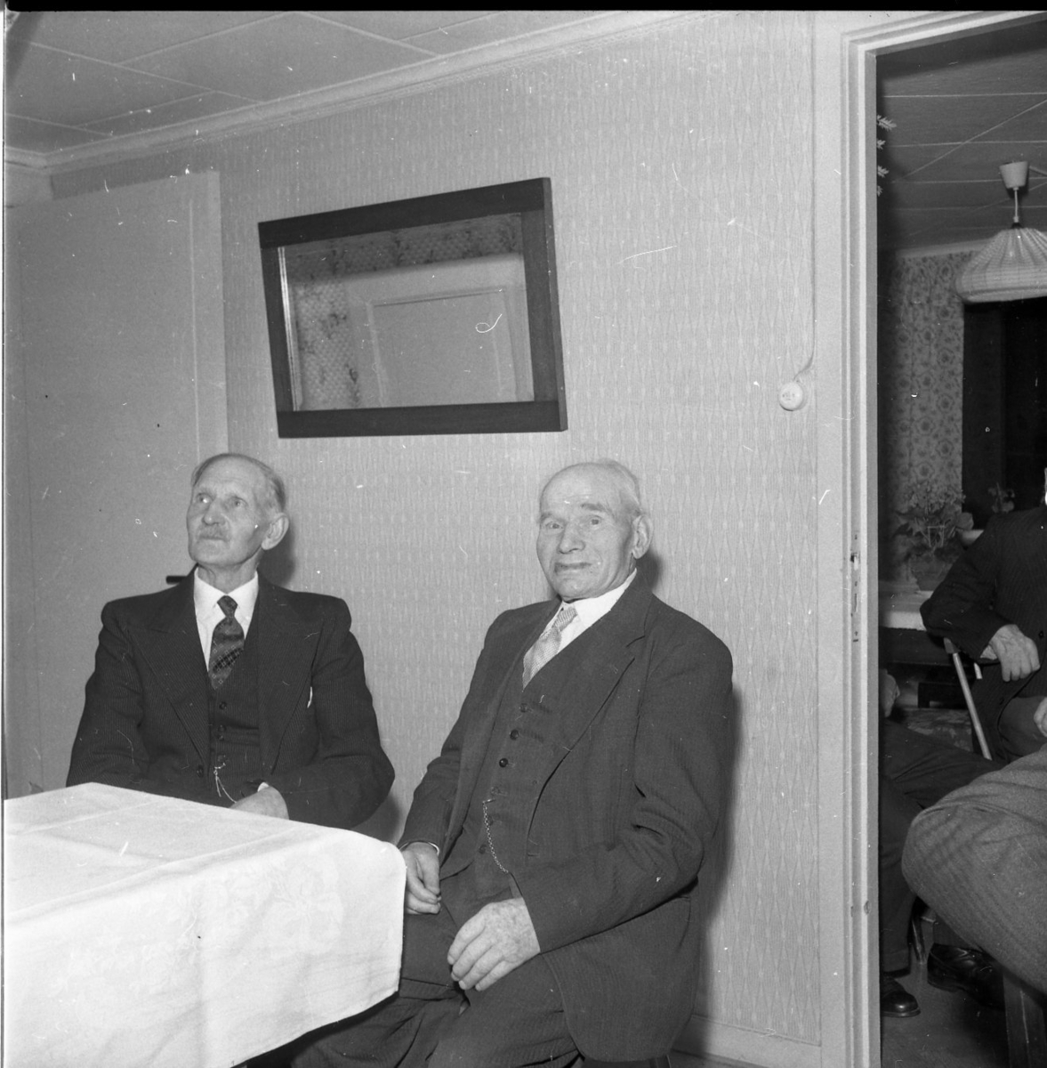 Två herrar klädda i slips och kavaj, under kavajen bär de väst. Kedjorna från fickur hänger ut ur de båda herrarnas fickor.