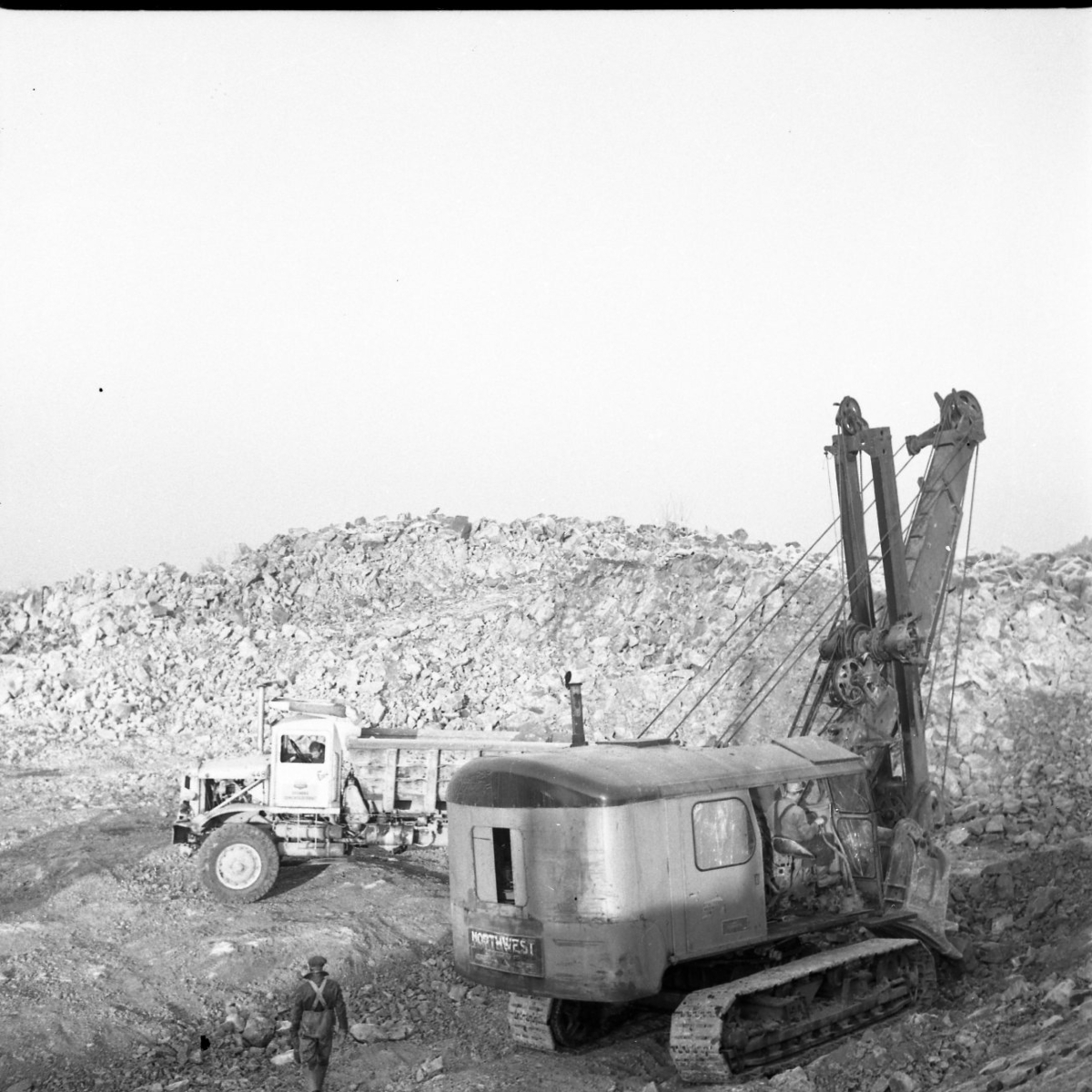 Bergrensning. En arbetare sitter i en grävmaskin som lastar upp bergrester på ett flak.