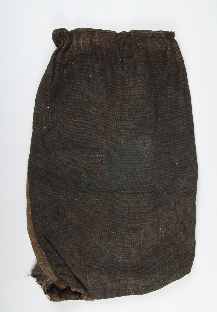 Textil av brunt tuskaftat lin. Enkelt "fållad" med brunt garn (bomull). Infärgad, beige i ursprung, ses i fåll. Trasig.