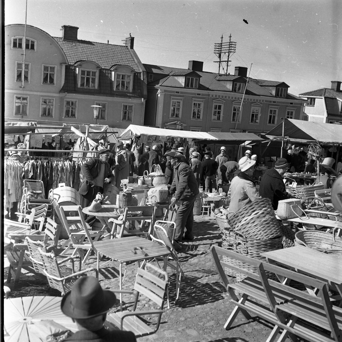 Marknad på Gränna torg. det säls bland annat bland annat kläder och korgar i flätat rotting. Mitt på torget står bord och stolar utställda.