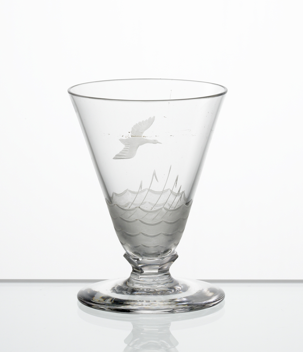 Design: Edward Hald.
Brännvinsglas. Konisk kupa med fasettslipad knapp mellan kupa och fot. Graverad flygande andfågel och, på kupans nedre del,
vass och vatten i vågor.