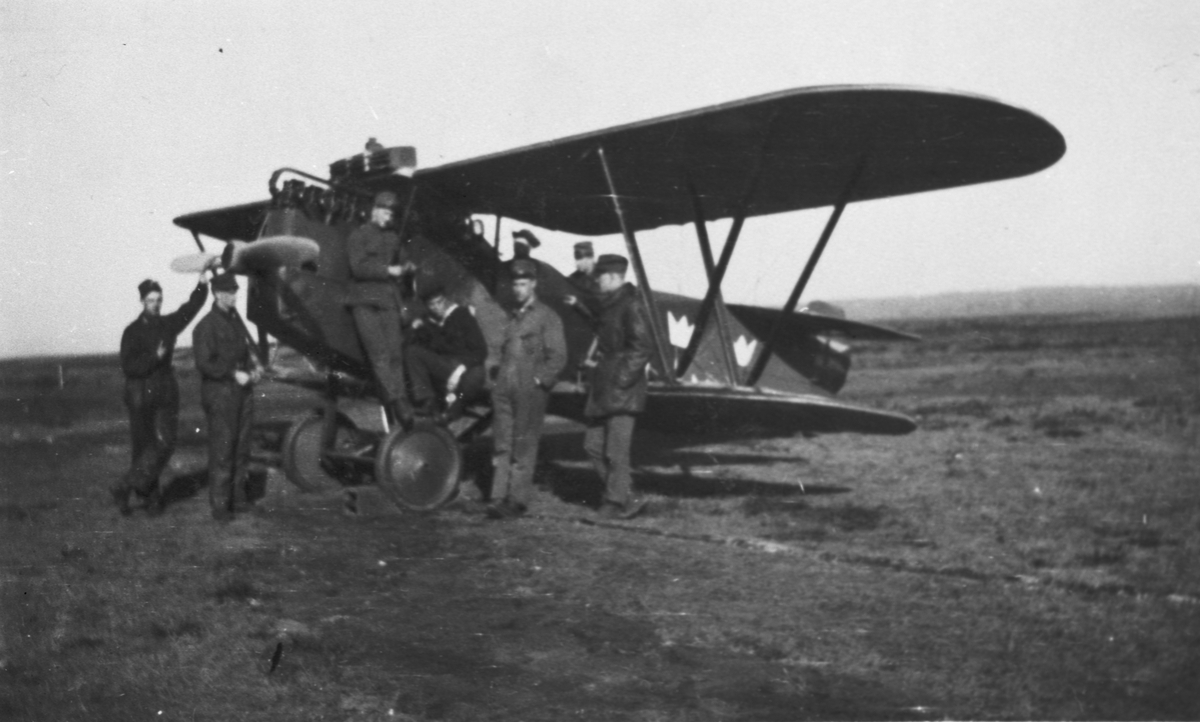 Flygplan Phönix C. I Dront ur Flygkompaniet står på ett flygfält. Åtta militärer vid flygplanet. 1919-1924.