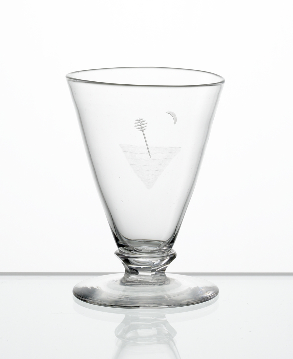 Design: Edward Hald.
Brännvinsglas, konisk kupa med graverat motiv bestående av sjömärke. Fasettslipad knapp mellan kupa och fot.