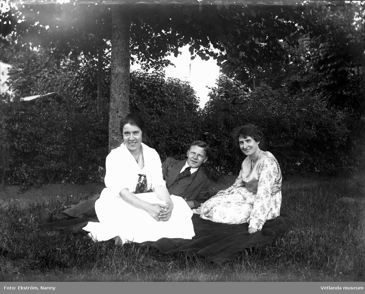 Två kvinnor och en man tillsammans med en hund i en trädgård. Personerna på bilden är troligtvis bekanta med fotografen, Nanny Ekström.