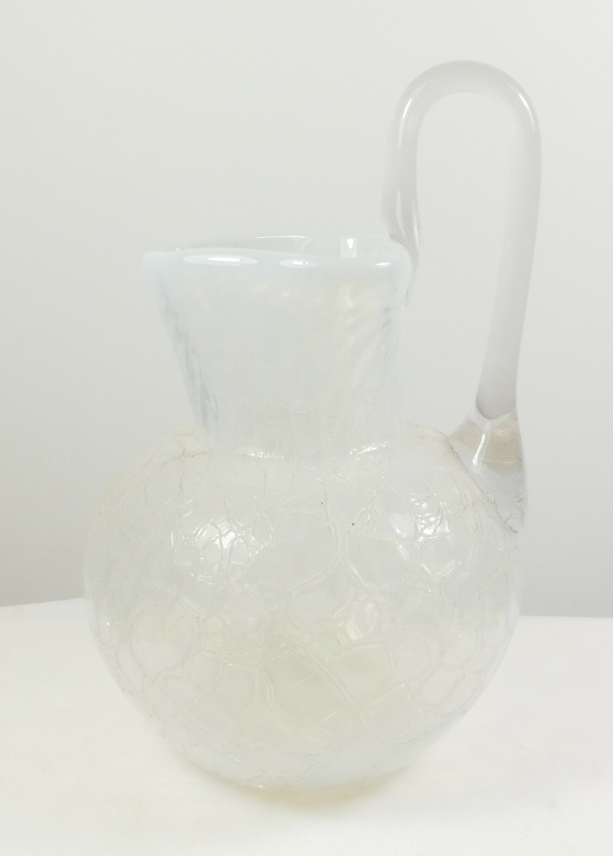 Rund mugge eller vase i glass. Over den runde bunnen er det en hjerteformet del med en hvit kant, et håndtak er festet på den ene siden