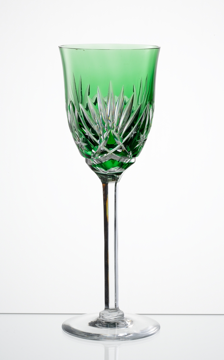 Design: Okänd. 
Rhenvinsglas, grön klockformad kupa med skärslipad dekor. Högt fasettslipat ben med slät fot.