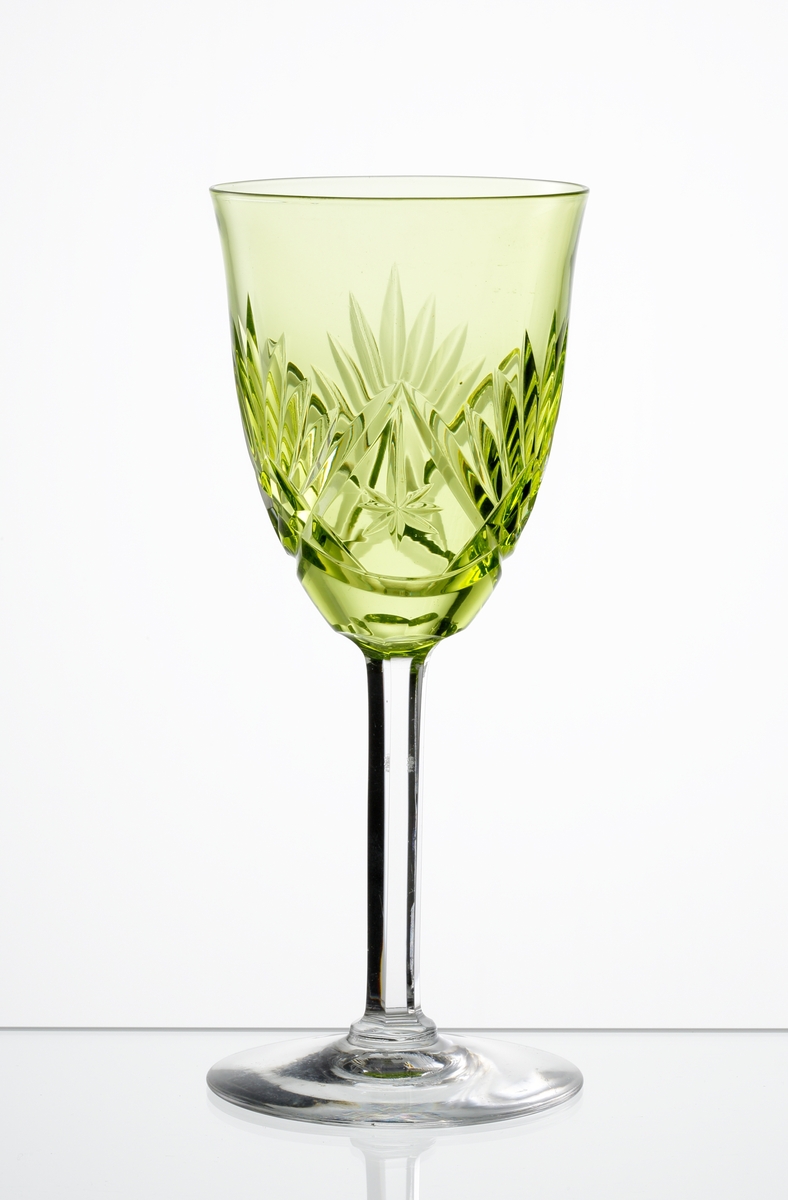 Design: Okänd. 
Vitvinsglas, gulgrön svagt klockformad kupa med skärslipad dekor. Högt fasettslipat ben med slät fot.