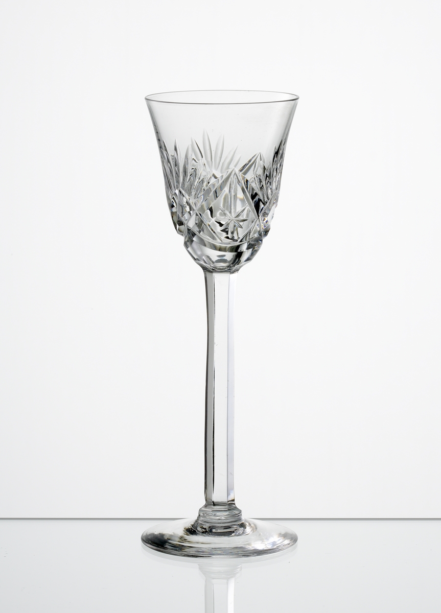 Design: Okänd. 
Brännvinsglas, svagt klockformad kupa med skärslipad dekor. Högt fasettslipat ben med slät fot.