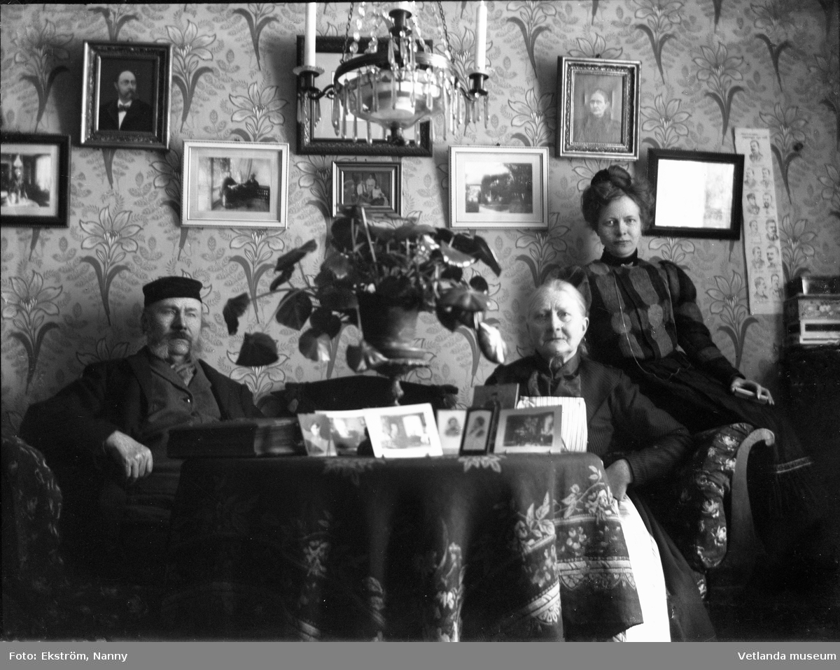 Tre personer i hemmiljö. Eventuellt är detta en bild på fotografen Nanny Ekström och hennes föräldrar, Johan och Christina.
