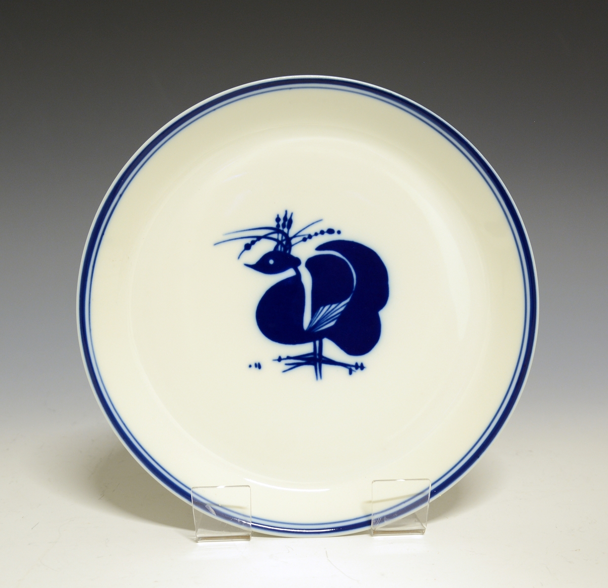 Flat tallerken av porselen med hvit glasur. Speilen dekorert med to stiliserte fugler og kantring i mørk blå farge. 
Modell 4281 "Ceylon" av Anne Marie Ødegaard, 1957. 
Dekor nr. 78141.