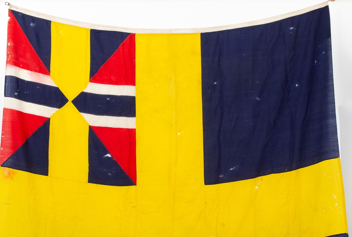 Svensk flagg med unionsmerke, "sildesalaten". Metallhempe. Møllspist og slitt.
Unionsmerket: 120 x 103

Givers datter opplyser at flagget var kjøpt på auksjon eller loppemarked på 1980 tallet. Det skal ha kommet fra båtbyggeriet på Kugrava i Son.
