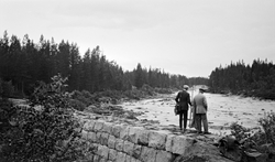 To personer på en demning av stenblokker. Ved elva Flisa, Ås