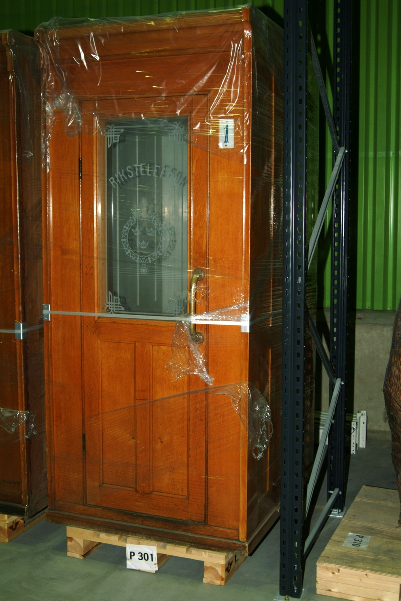 Talhytt för betjänad telefonstation, hytten märkt "1". Framsida i polerad ek, glas i dörr med riksvapen och texten "Rikstelefon".