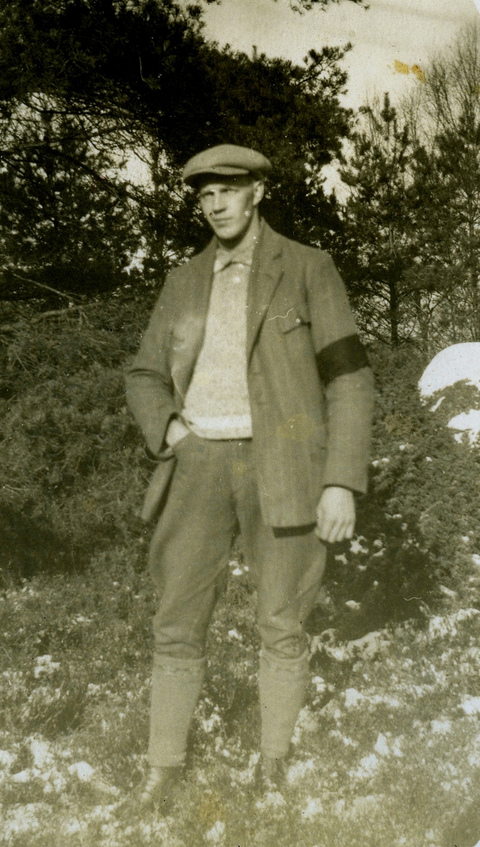 En okänd man, klädd i kostym och med sorgband på vänster arm, står på tomten vid Kållered Stom "Nygård" okänt årtal.