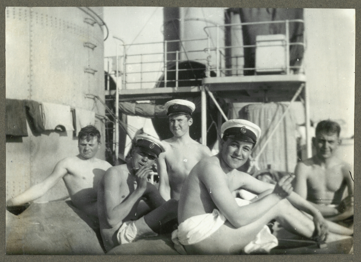 Bilden visar sjömän som vila på däcket av en torpedbåt efter en bad tur. Pojkarna täcker sin nakenhet nödtorftig med en handduk men bär uniformsmössa och röker cigaretter.
