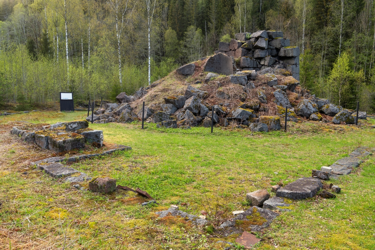 Ruinen etter Fritzøe jernverks masovn på Moholt i Siljan. Fotografiet er tatt fra sør. Det rennende elvevatnet som drev blåsebelgene som tilførte den metallurgiske prosessen som foregikk her nok oksygenrik luft til at temperaturen inne i ildstedet ble høy nok, er her skjult bak ruinen og krattskogen langs elvebredden.

Masovnteknologien ble innført i Norge tidlig på 1600-tallet. Det dreide seg om digre, høye steinovner som hadde noenlunde runde brennkamre. Når en slik ovn skulle settes i drift, ble den fylt med trekol, som ble antent og fikk stå å gløde 3-4 uker før konstruksjonen var varm nok. Tilstrekkelig høy varme ble oppnådd ved hjelp av oksygentilførsel fra et par blåsebelger som ble drevet ved hjelp av vannkraft fra elva.  Etter at ovnen hadde stått full av glødende trekull et par uker, var murverket varmt nok til at den metallurgiske produksjonsprosessen kunne starte. Det ble gjort ved «påsettinga» av trekol og malm, lag for lag, fra «krona», overkanten på masovnmuren. Slik kunne masovnen holdes i kontinuerlig drift gjennom et par år før det ble nødvendig å avslutte fyringa og skifte ut steinene i de mest varmeeksponerte delene av brennkammeret. Dette forutsatte naturligvis at verket hadde gode lagere av malm og trekol. Mens prosessen pågikk ble det stadig tappet råjern gjennom et hull - «stellet» - i den nedre delen av ildstedet. Dette jernet kunne enten brukes i støpejernsprodukter umiddelbart, eller det kunne bearbeides videre til smidigere smijern i en «hammer».  På Moholt ble det bygd et hammerverk tidlig i 1730-åra. Hit transpporterte man forholdsvis små volumer av råjern fra Fritzøe-verkets hovedanlegg i Larvik med ferger over innsjøen Farris, i stedet for å frakte store volumer av trekull den motsatte vegen. Under napoleonskrigene tidlig på 1800-tallet økte etterspørselen etter jern. I denne perioden hadde det vist seg vanskelig å skaffe nok trekull til masovnen i Barkevik i Brunlanes. Derfor bestemte ledelsen i Fritzøe-verket at noe av råjernproduksjonen skulle flyttes til Moholt, der man hadde bedre tilgang på trekull fra skogene i Siljan. Dette var bakgrunnen for at man bygde den masovnen vi ser på dette fotografiet i perioden 1809-1817. Årsaken til at byggeprosessen tok så lang tid var at de varmeresistente steinene som skulle være i området rundt stellet måtte importeres, noe som var vanskelig i en periode med krig og blokader av skipsfarten. Masovnen på Moholt var i drift i en 50-årsperiode, fra 1817 til 1867. Den var omgitt av ei smeltehytte, en bordkledd bindingsverkskonstruksjon, som vi ser noen av fundamentene til i forgrunnen på dette bildet. Dette kulturminnet er tilgjengeliggjort for interesserte med informasjonsskilt og tilstøtende rasteplass. Klatring i ovnsruien er ikke ønskelig. Den er derfor skjermet ved hjelp av et enkelt kjettingstengsel. 

Litt mer historisk informasjon om den metallurgiske virksomheten på Moholt finnes under fanen «Opplysninger».