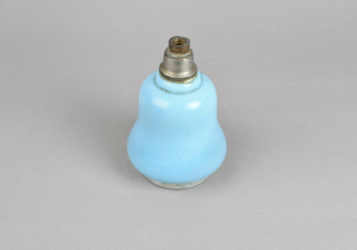 Parfymeflakong med klokkeform og plass for dusjknapp på toppen. Korpus er av blåfarvet porselen, toppen og fotranden er i blankt metall.