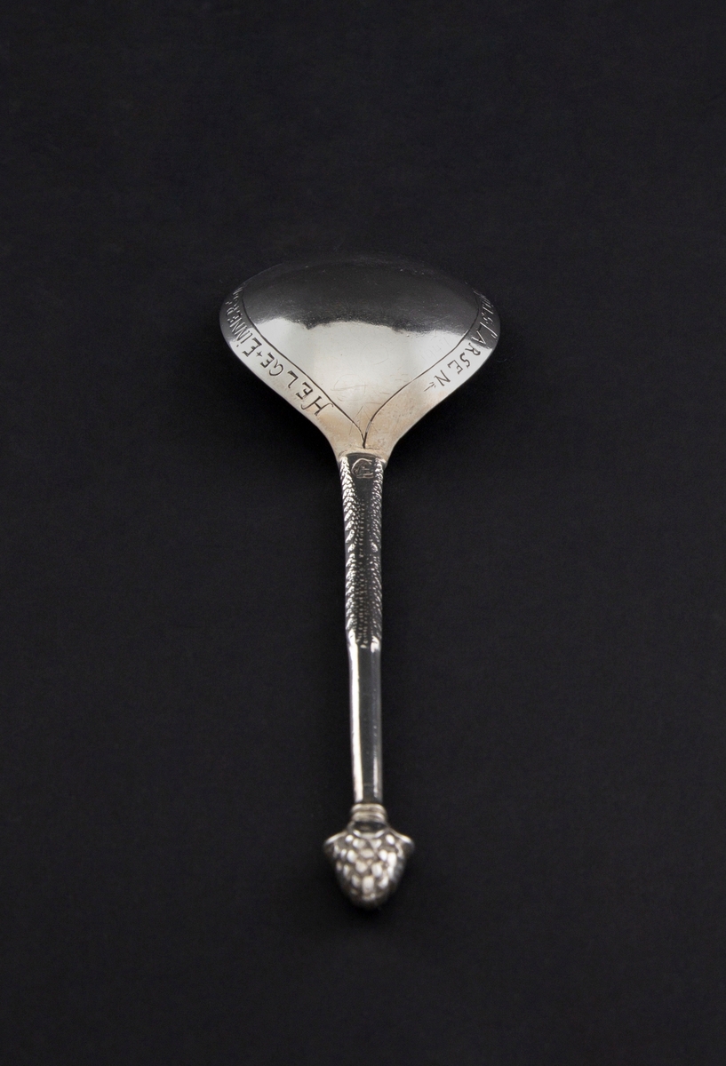 Drueskje av sølv med dråpeformet skjeblad og kort skaft med drueklase i enden.