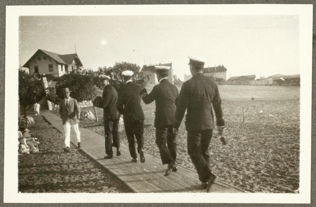 Bilden visar fyra befäl från Fylgia som går på en plankväg vid stranden av Swakopmund.