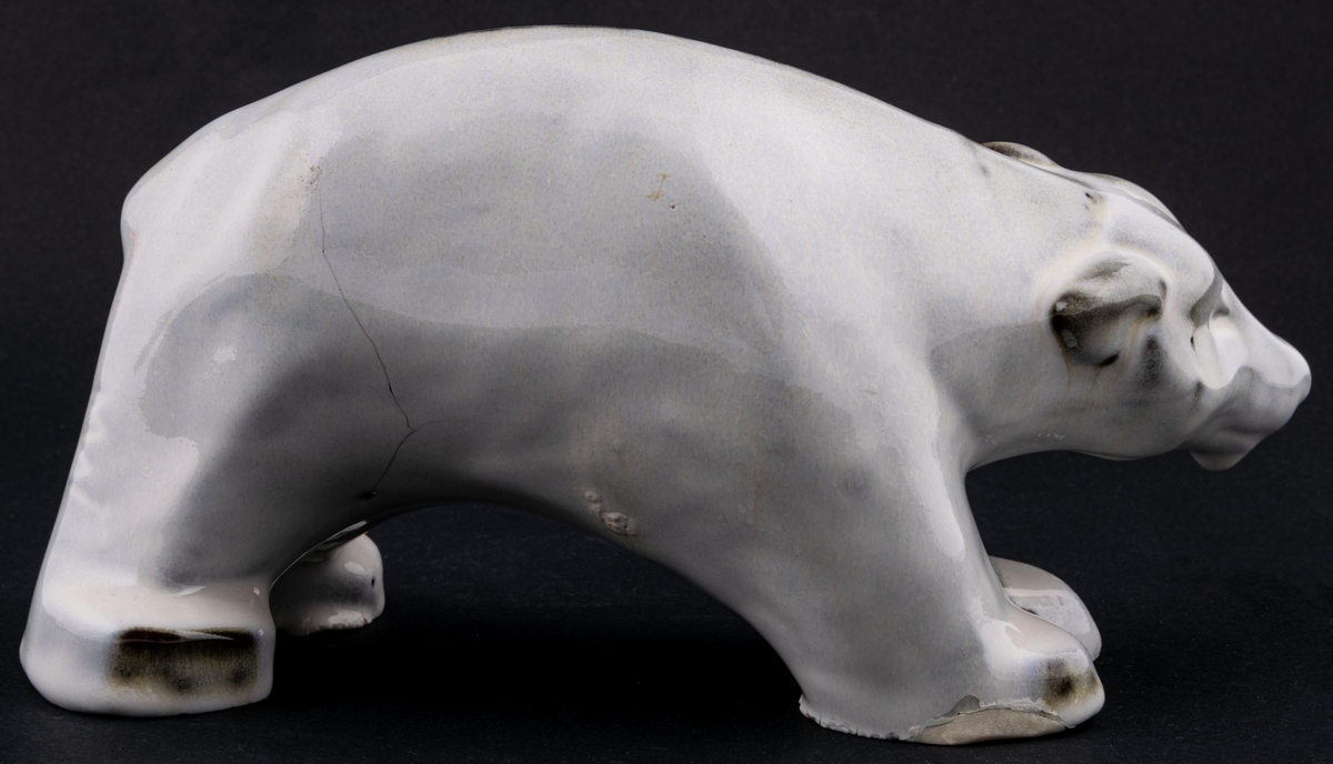Figurin föreställande stående isbjörn, röd stengodslera, vit blank glasyr. Formgiven av Maggie Wibom för Gefle 1933-43, signerad med initialer på höger bakben. Inga fabriksstämplar.