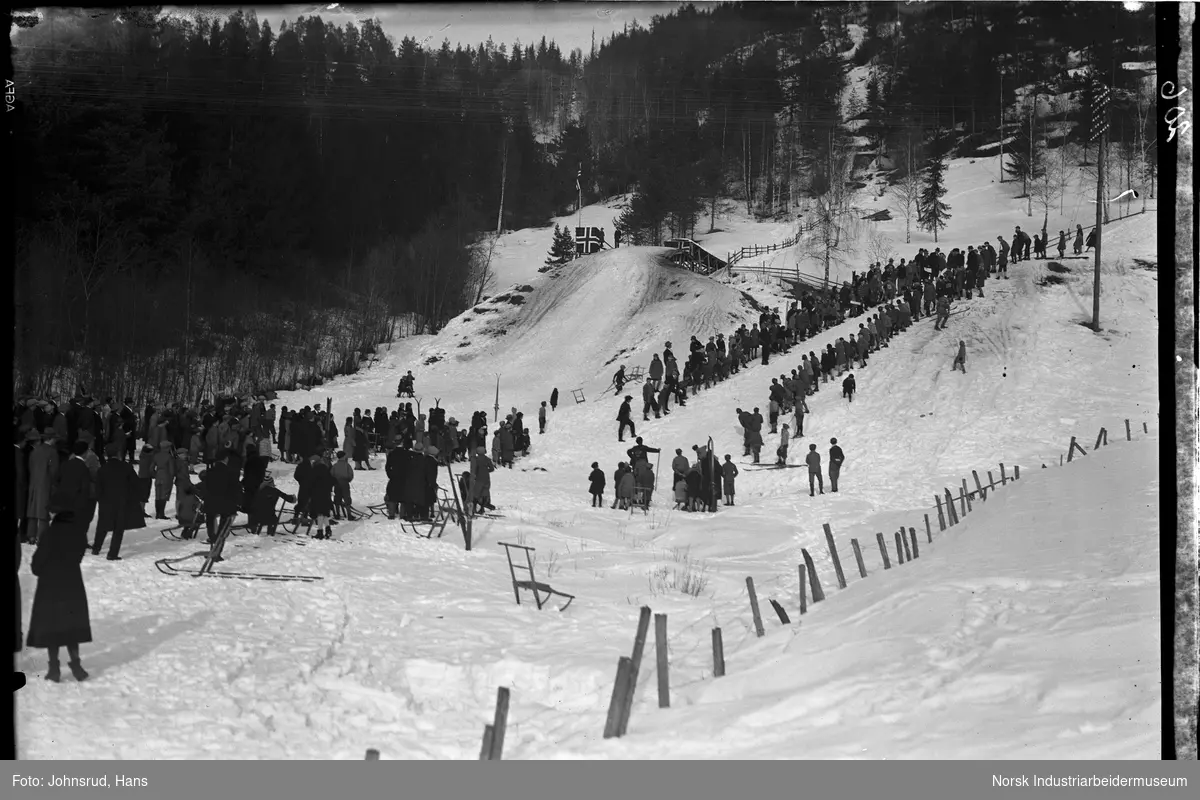 Jernbanens idrettslag arrangerer hoppkonkurranse. Folkemengde samlet i bakken for å se skihopp.