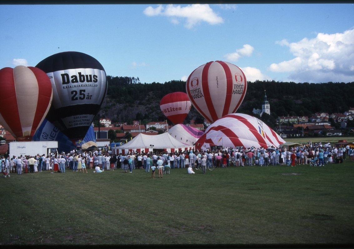 Luftballonger fylls och lyfter från en gräsplan. En stor publik.