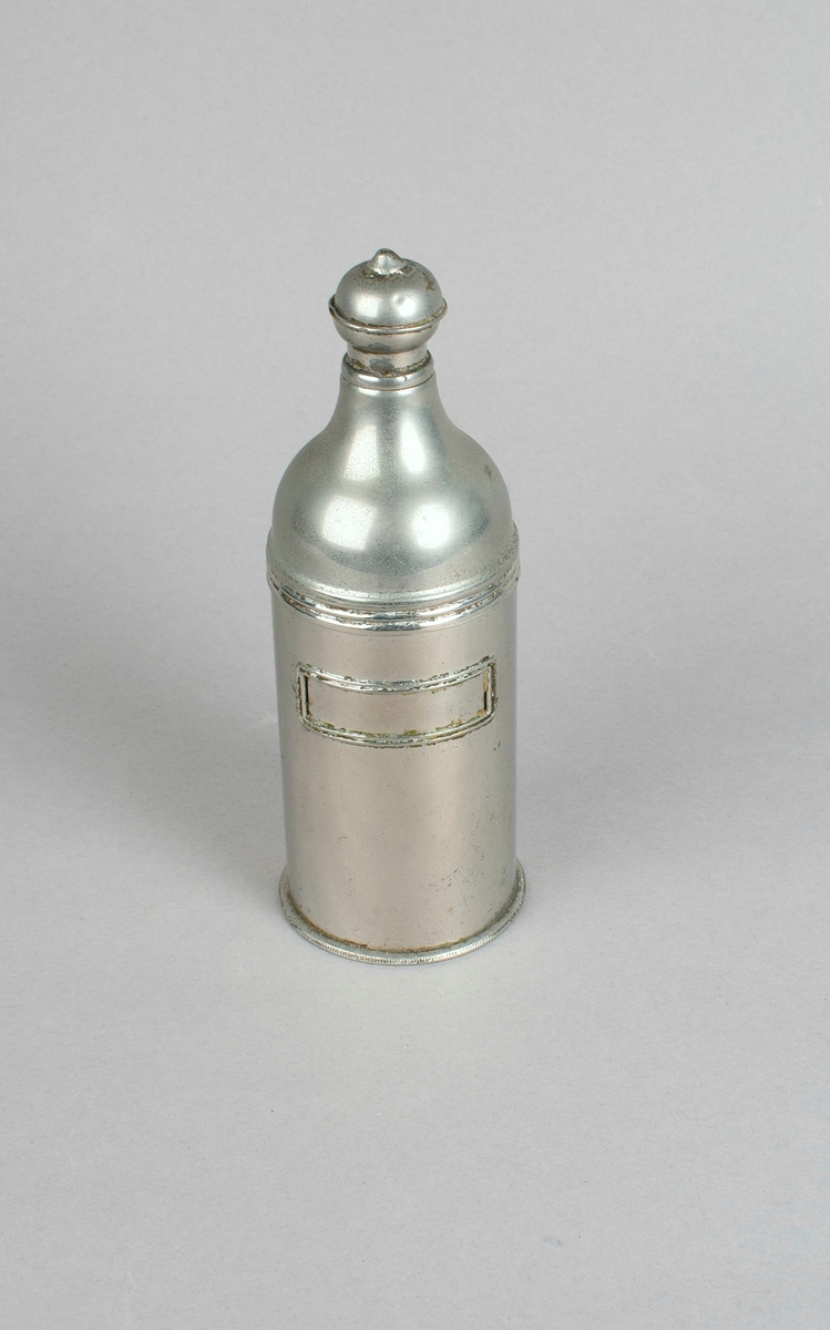 Sylinderformet flaske med kort hals og halvkuleformet dynketopp med lite hull. Innrammet rektangulært felt til etikett.