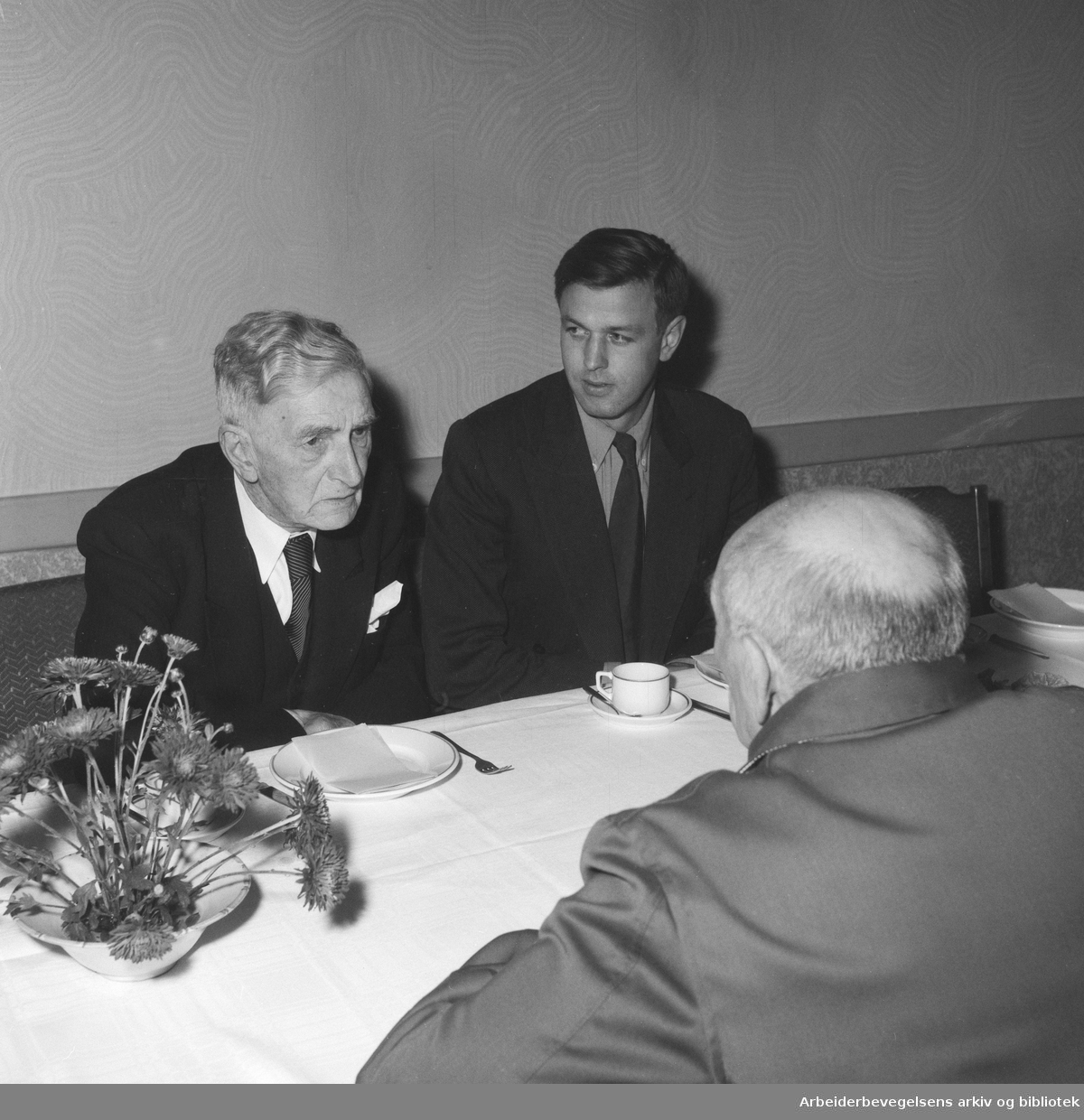 Johan Falkberget fyller 75 år. Arbeiderbladets redaksjon samlet på restaurant Stratos. Falkberget og journalist Per Wiedsvang. Martin Tranmæl med ryggen til. Oktober 1954.